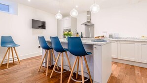 A modern kitchen with white cabinets, a central island, and blue bar stools. - 5 Bed in Matlock Bath (oc-85188) (Matlock Bath)