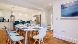 A modern kitchen with white cabinets, a stainless steel range hood, and a dining area with a white table set for four. - 5 Bed in Matlock Bath (oc-85188) (Matlock Bath)
