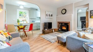 Ein Wohnzimmer mit Kamin, ein Essbereich mit Tisch und Stühlen sowie eine Küche im Hintergrund.