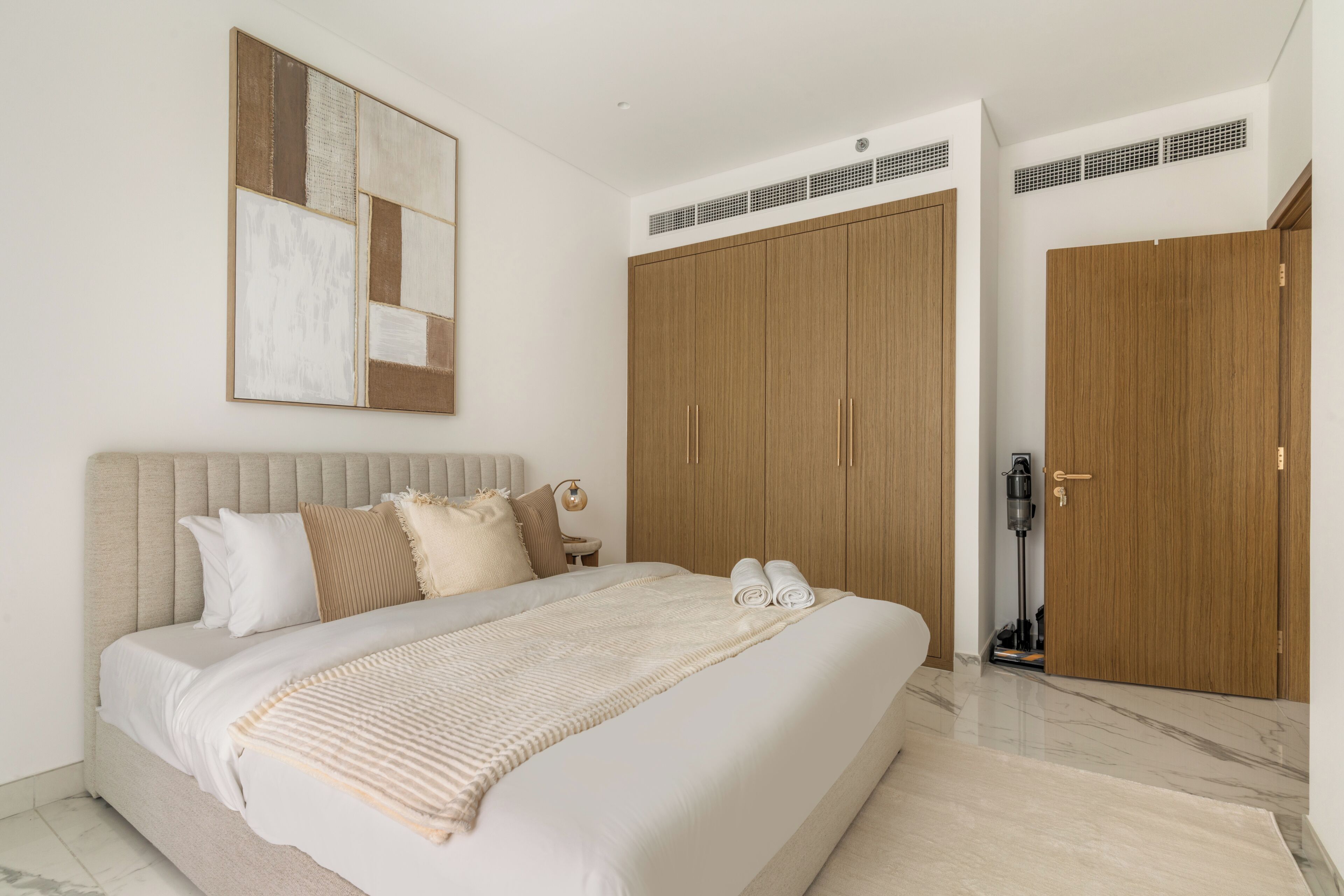 Een moderne slaapkamer met een groot bed, een houten garderobe en een ventilatie rooster in het plafond.