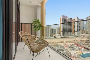 A balcony with a wicker chair, a potted plant, and a cityscape view. - Silkhaus Azizi Riviera67 (Dubai)