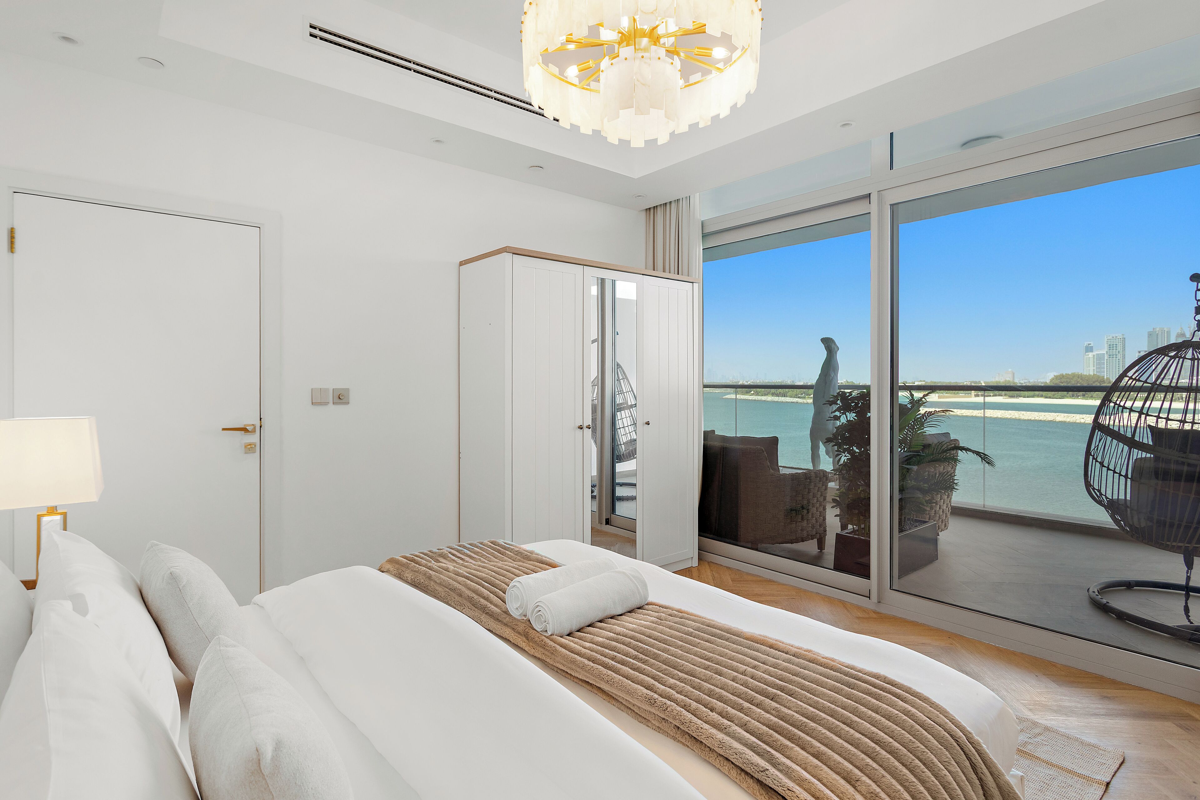 A modern bedroom with a large bed, a view of the sea, and a balcony with outdoor furniture.