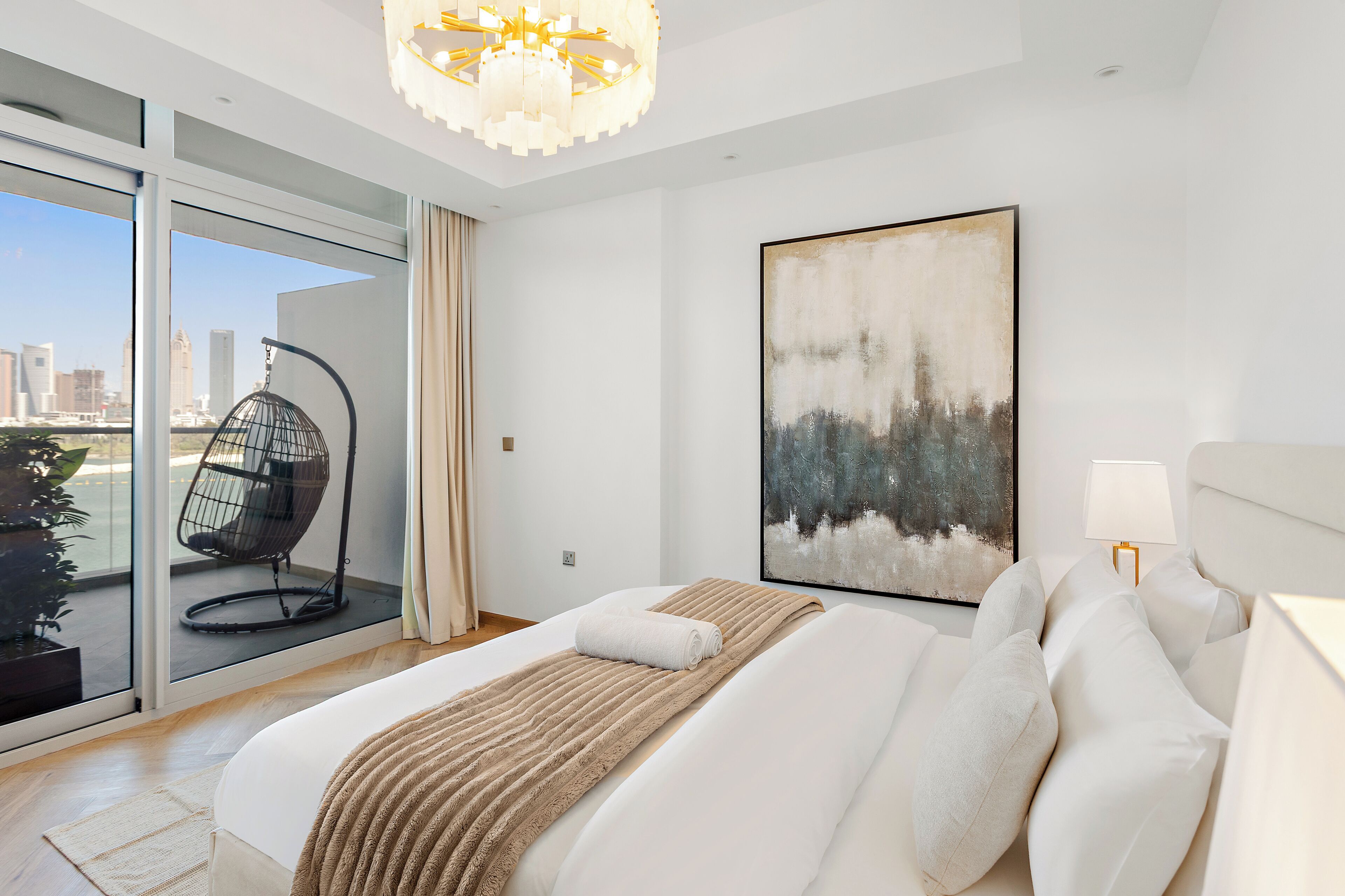 A modern bedroom with a large bed, a city view, a hanging chair, and a painting.