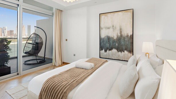 A modern bedroom with a large bed, a city view, a hanging chair, and a painting. - Silkhaus Azure Residences (Dubai)