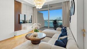 A modern living room with a large window, a chandelier, a sofa, and a flat-screen TV. - Silkhaus Azure Residences (Dubai)