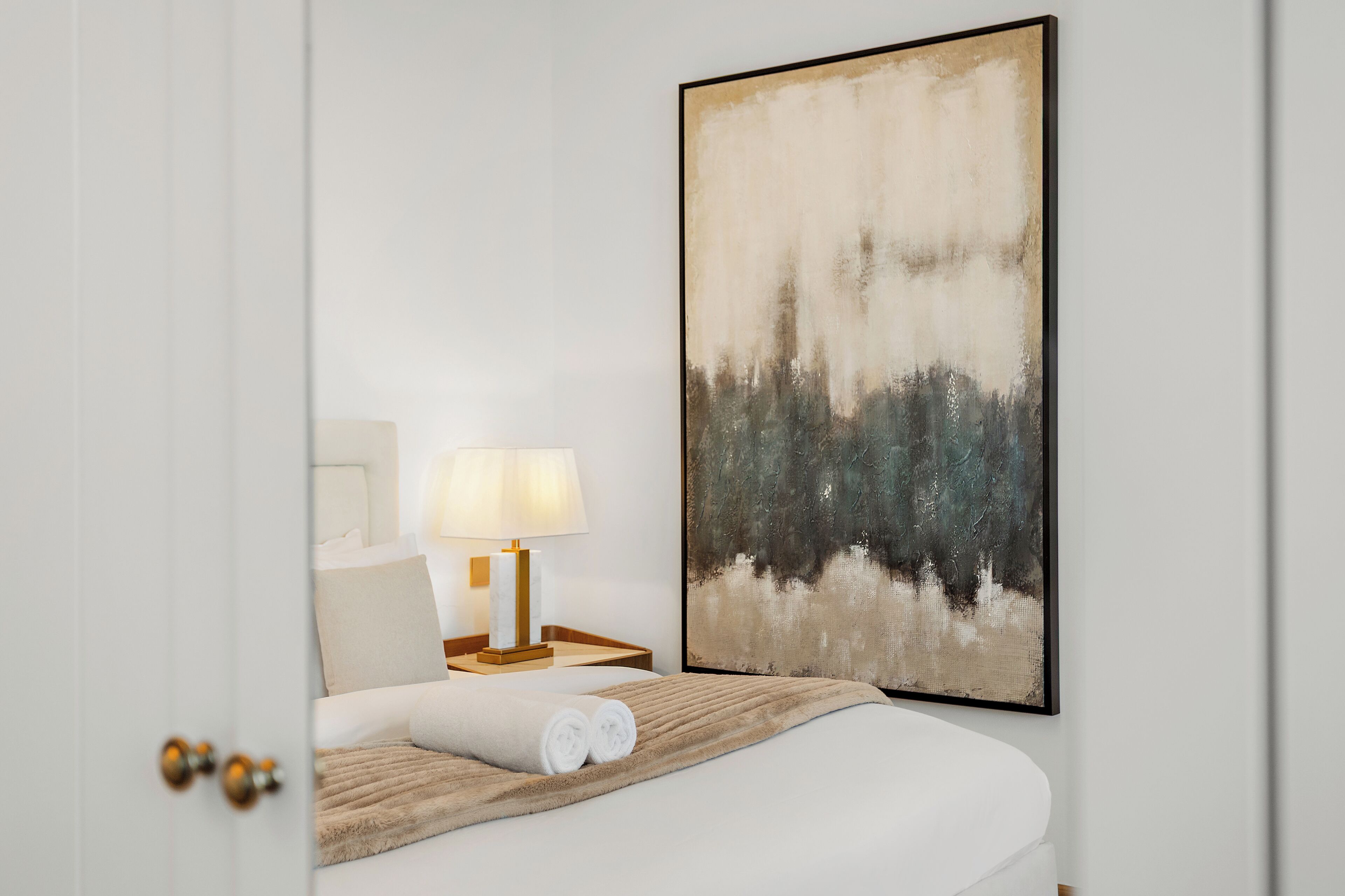 Une chambre d’hôtel avec un lit, une lampe de chevet, un grand tableau abstrait et une porte.