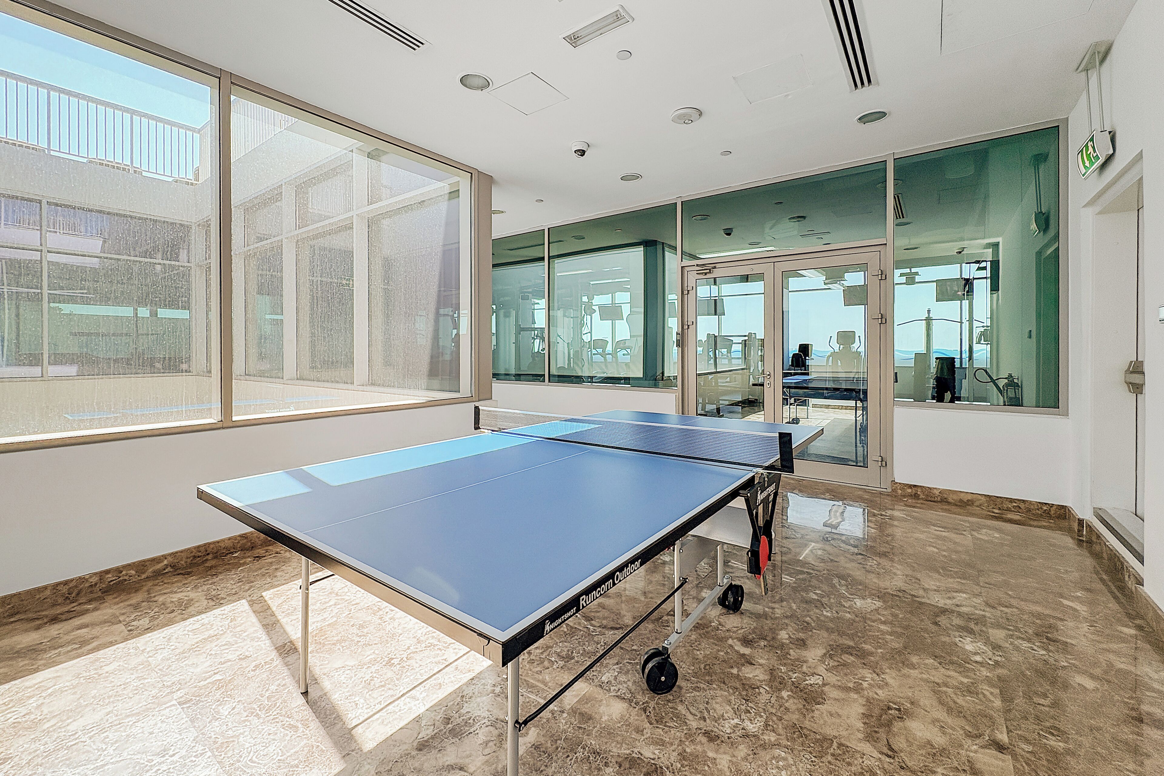 A ping pong table in a room with large windows and a glass door leading to another room.
