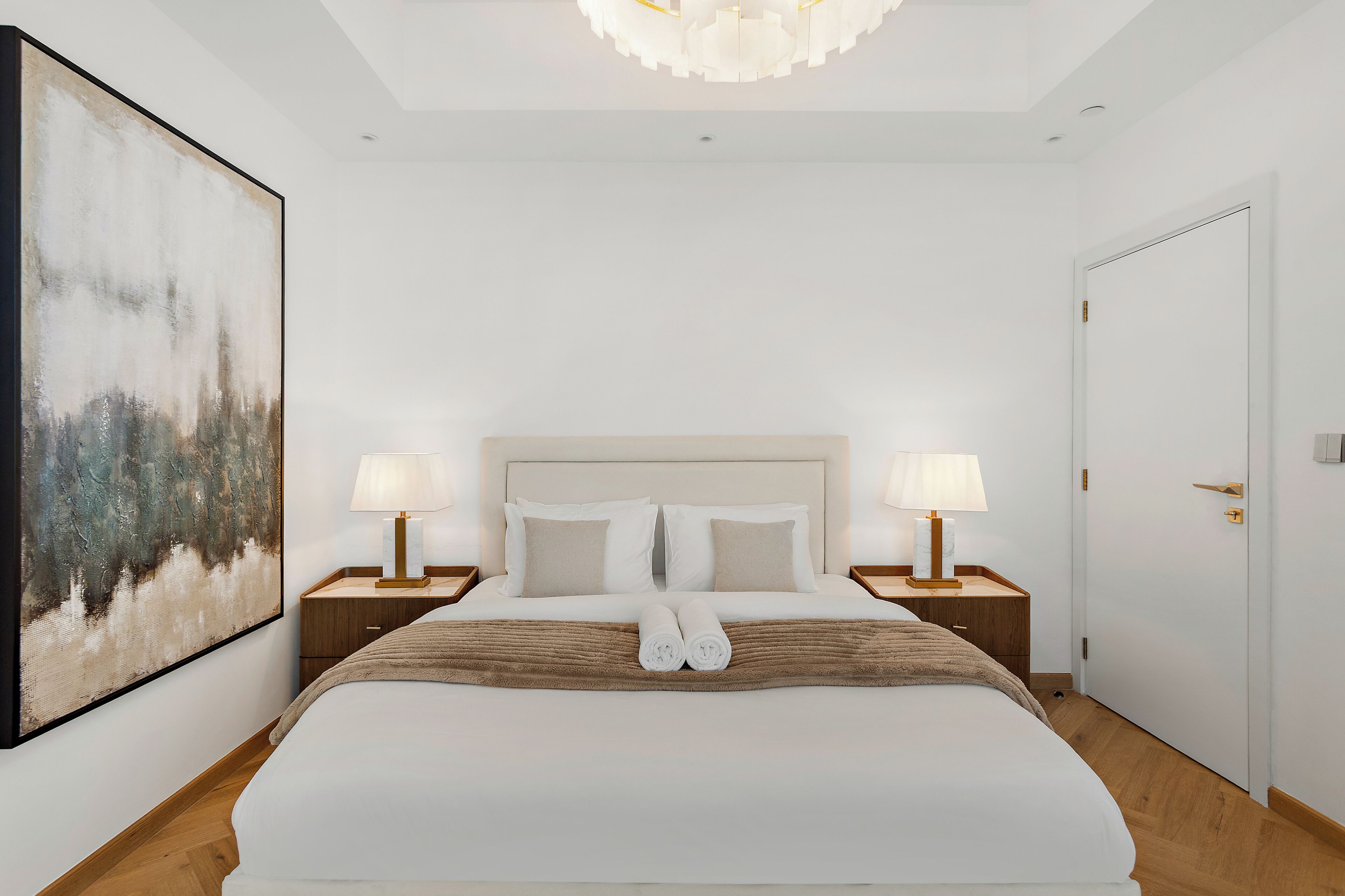 A hotel room with a large bed, two bedside tables, a nightstand, a door, and a painting on the wall.