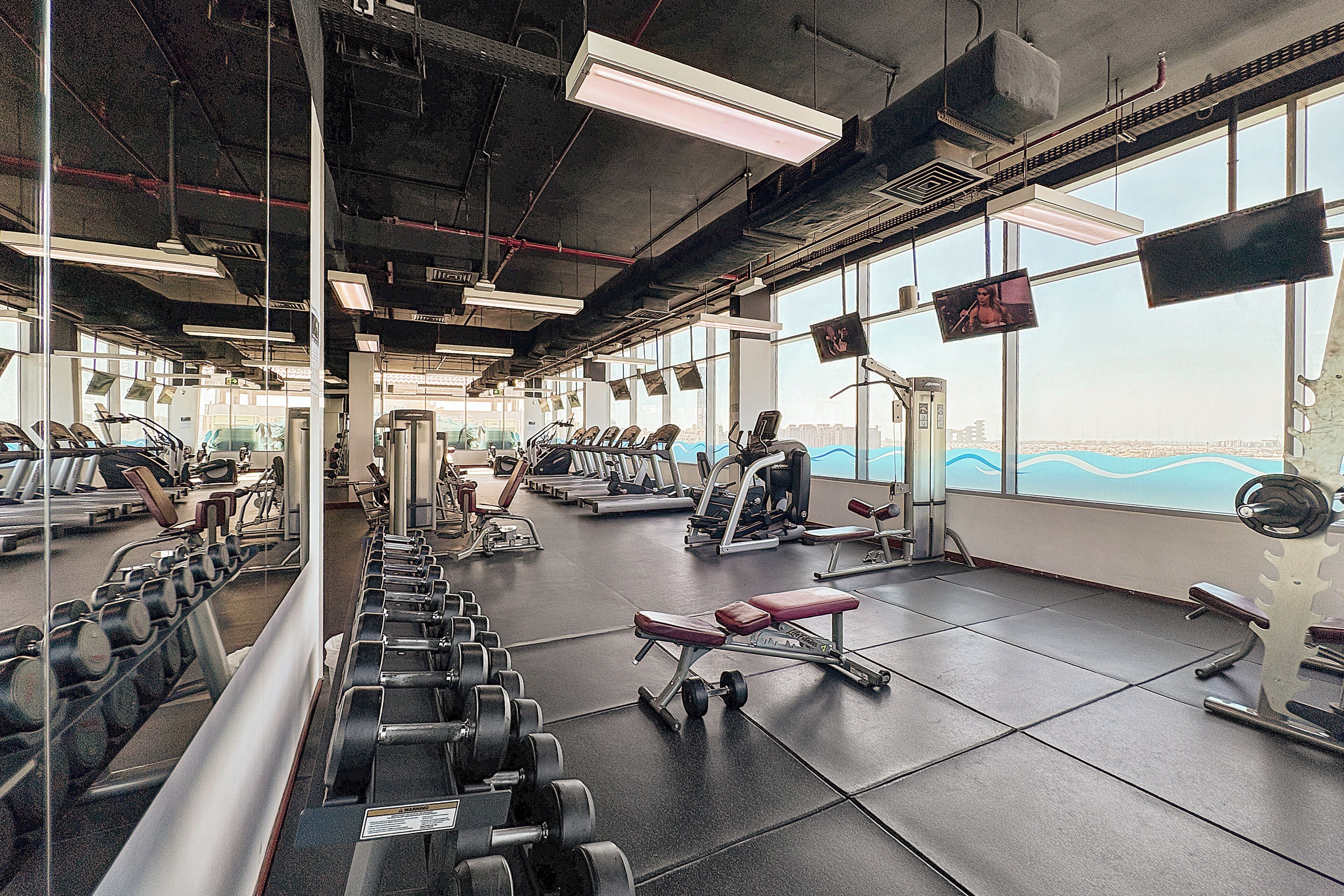 A gym with various exercise equipment, large windows, and a view of the cityscape.