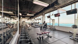 A gym with various exercise equipment, large windows, and a view of the cityscape. - Silkhaus Azure Residences (Dubai)