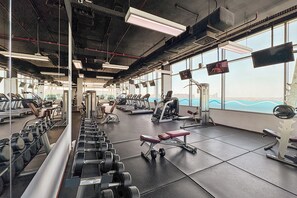 Ein Fitnessstudio mit diversen Trainingsgeräten, großen Fenstern und Blick auf die Skyline der Stadt.