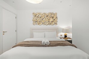 Ein Hotelzimmer mit einem großen Bett, einem Kopfteil, einem Wandbild, einem Nachttisch mit Lampe und einer Tür.