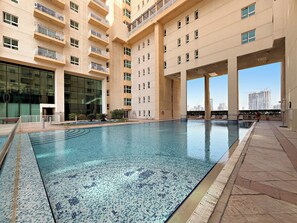 A swimming pool with a tiled floor, surrounded by a building with multiple balconies and large windows. - Silkhaus Centrium (Dubai)