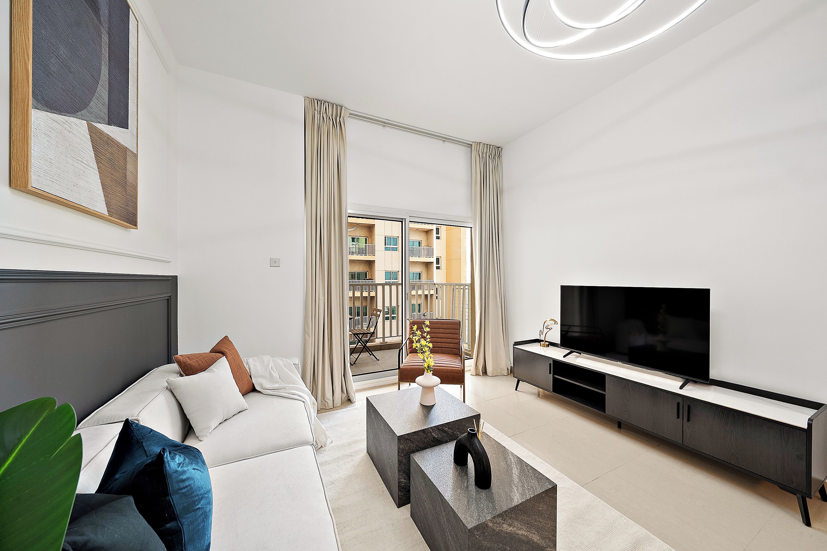 A modern living room with a sofa, coffee table, TV, and a view of a balcony with a building in the background.
