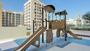 A playground with a slide and climbing structures, set against a backdrop of modern buildings and a clear sky. - Silkhaus Hyde Walk (Dubai)