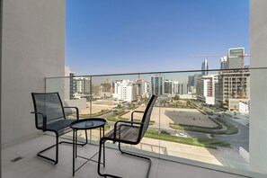 Ein Balkon mit zwei Stühlen und einem kleinen Tisch mit Blick auf eine Stadtlandschaft, in der moderne Gebäude und Baukräne zu sehen sind.