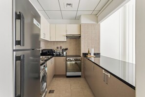A compact kitchen with a stainless steel refrigerator, a built-in oven, a washing machine, and a microwave. - Silkhaus Polo Residence (Dubai)