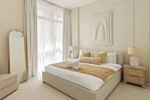 A hotel room with a large bed, a side table, a mirror, and a view of the outdoors. - Silkhaus Polo Residence (Dubai)