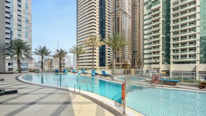 Piscina no terraço com espreguiçadeiras e palmeiras, cercada por edifícios altos.