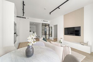 A modern living room with a dining area, a flat-screen TV mounted on a wooden panel, and a kitchen visible in the background. - Silkhaus Torche Tower (Dubai)