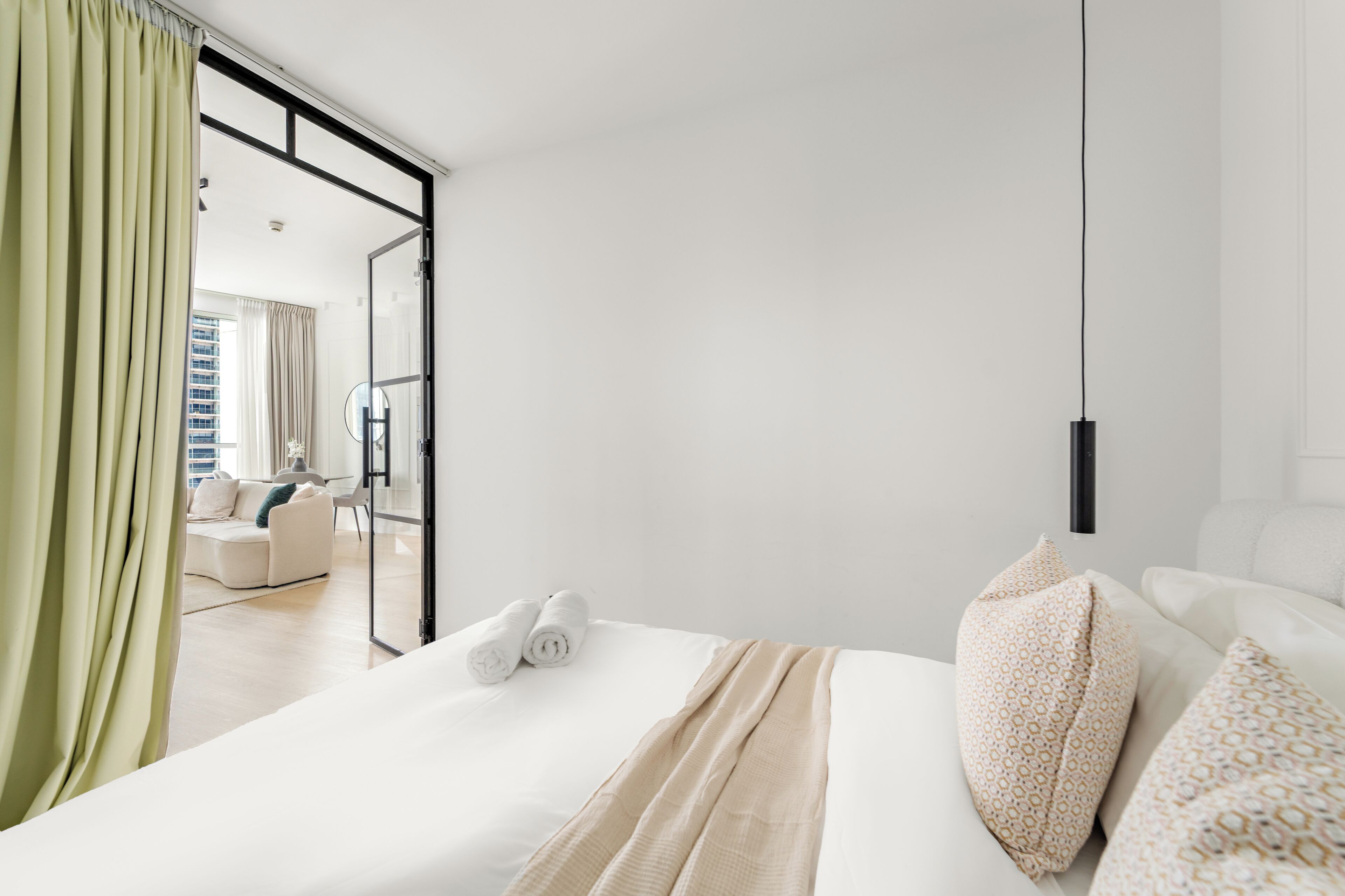 Une chambre d’hôtel moderne avec un lit, une vue à travers une porte vitrée et un coin repas visible au fond.