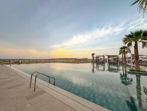 Una piscina infinita con vistas al paisaje desértico, una palmera y un área de descanso con sombra.
