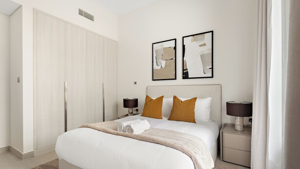 Habitación de hotel con cama, dos lámparas de noche, mesita de noche, ventana con cortinas y puerta.