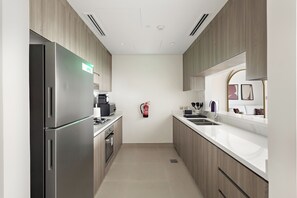 A modern kitchen with stainless steel appliances, wooden cabinets, and a white countertop. - Silkhaus Yas Golf Collection (Abu Dhabi)