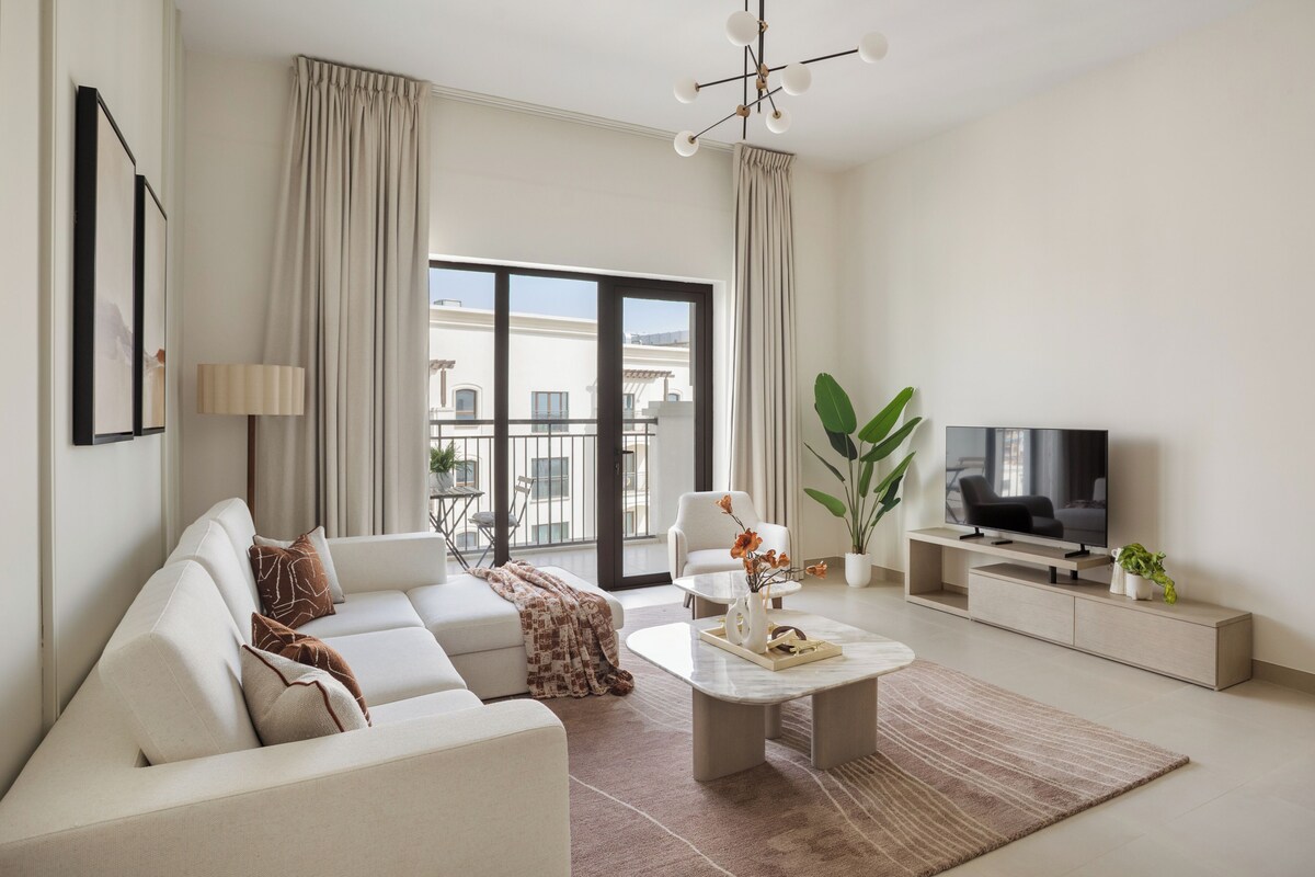 A modern living room with a sofa, coffee table, TV, and large windows.