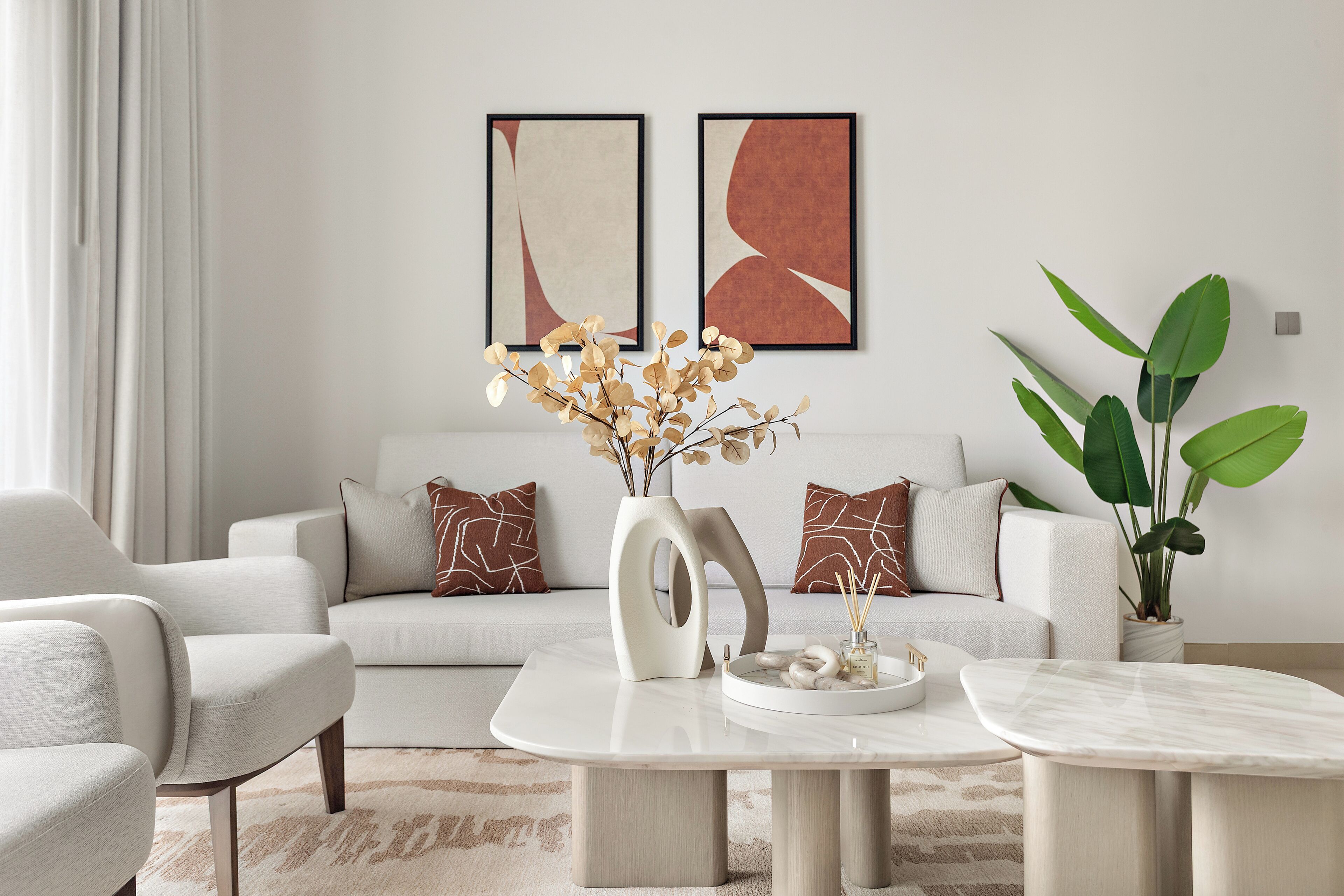 A modern living room with a sofa, armchairs, a coffee table, and decorative elements like a vase with dried flowers and a potted plant.