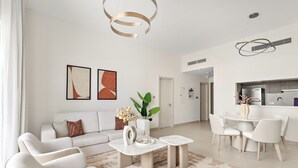 Una sala de estar moderna con sof á, mesa de centro y una zona de comedor con sillas. Se ve una cocina al fondo.