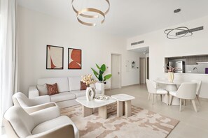 A modern living room with a sofa, coffee table, and a dining area with chairs. There is a kitchen visible in the background. - Silkhaus Yas Golf Collection (Abu Dhabi)