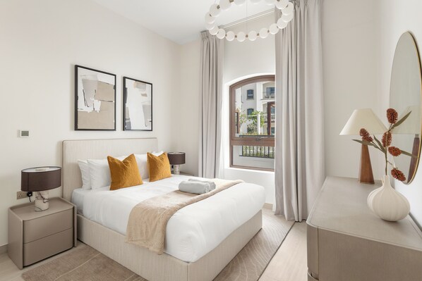 Habitación de hotel con cama, mesita de noche, lámpara, espejo y ventana con cortinas.