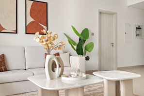 A modern living room with a sofa, two side tables, a vase with dried flowers, a potted plant, and abstract art on the wall. - Silkhaus Yas Golf Collection (Abu Dhabi)