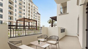 Un balcón con mobiliario de mimbre, una mesa y vistas a un edificio de gran altura.
