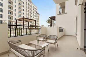 A balcony with wicker furniture, a table, and a view of a high-rise building. - Silkhaus Yas Golf Collection (Abu Dhabi)