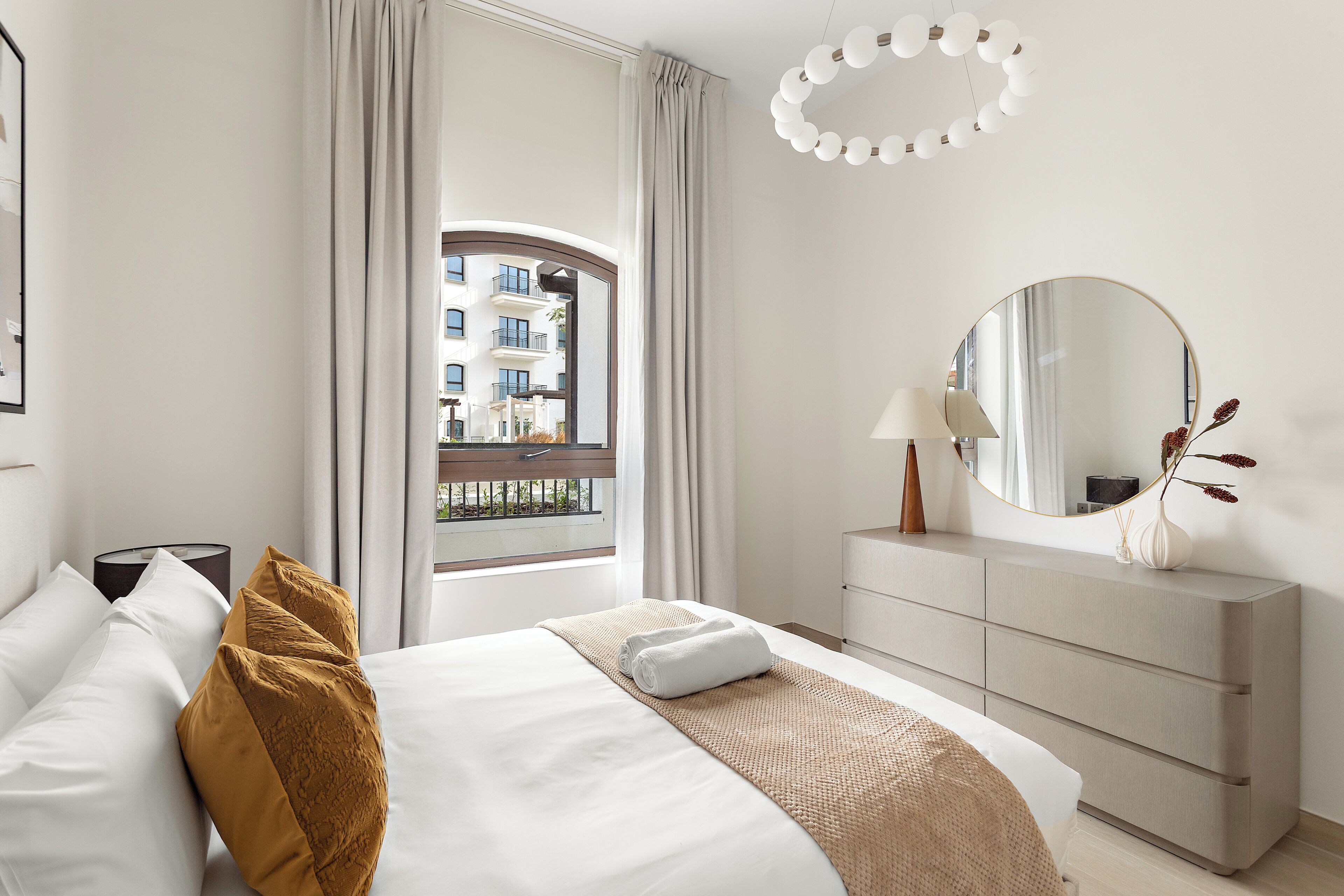 Une chambre d’hôtel avec un lit, une commode, un miroir et une fenêtre donnant sur un immeuble.