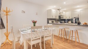Uma cozinha moderna com armários brancos, uma área de jantar com mesa e cadeiras brancas, e um pequeno balcão com banquetas.