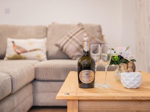 A bottle of wine and two glasses on a wooden table in a living room with a sofa and decorative pillows. - 3 Bed in Keswick (oc-sz217) (Threlkeld)