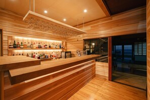 Zona de bar con estantes de madera llenos de botellas, una barra y un área de estar con vistas.