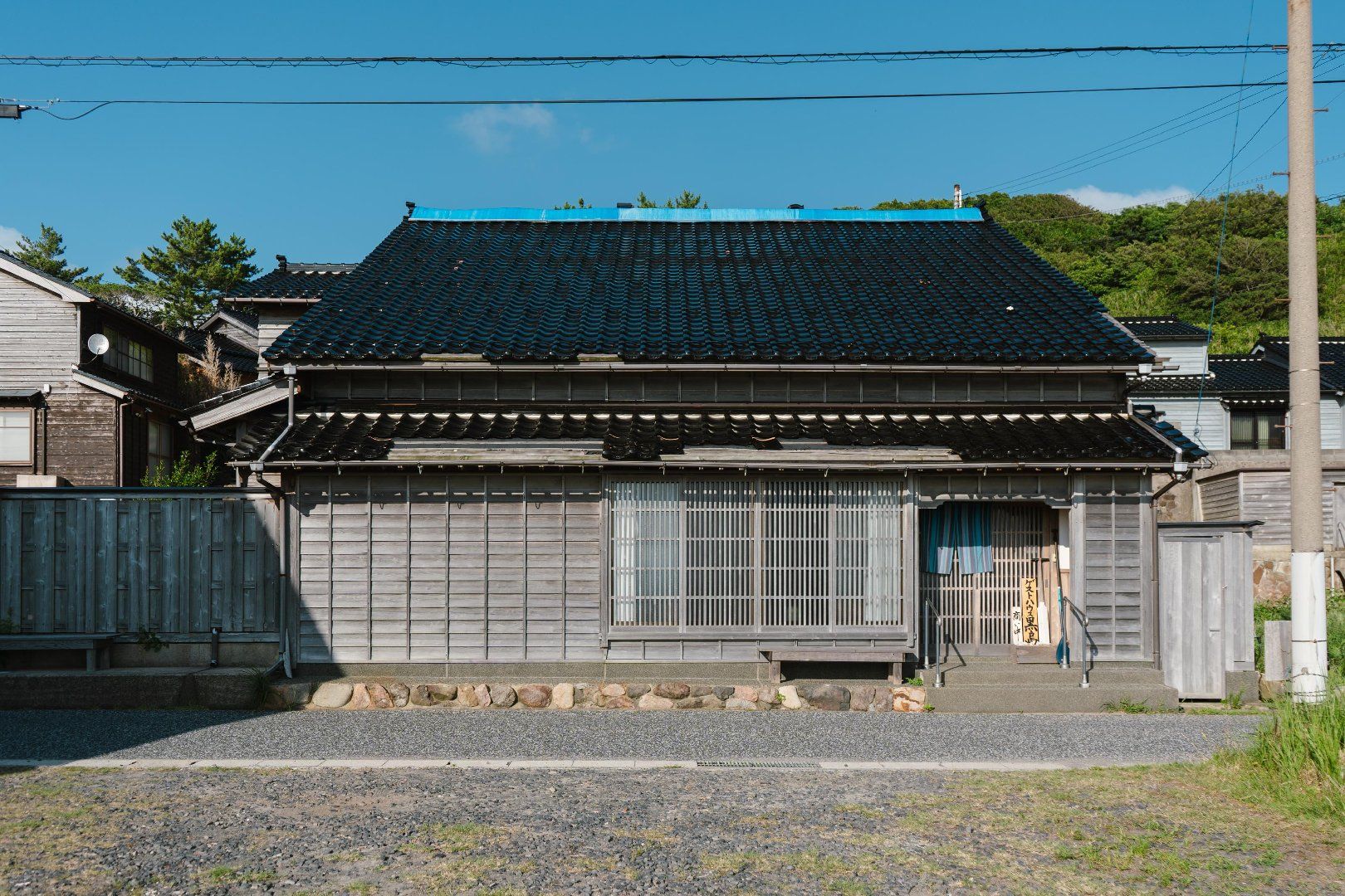 A traditional Japanese building with a tiled roof, wooden walls, and a gravel driveway.