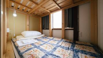 A bedroom with a wooden ceiling, a bed with a floral quilt, a bedside lamp, and a window with curtains.