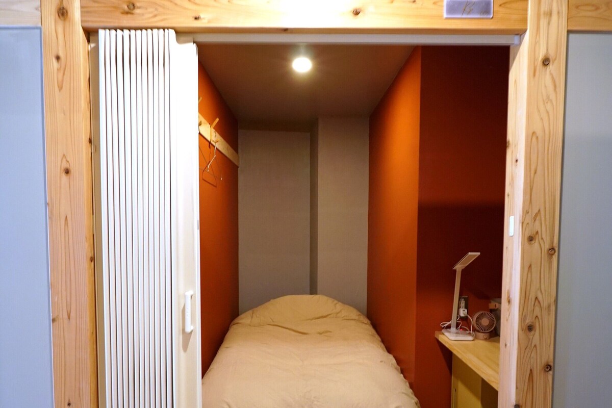 A bedroom with a bed, a desk with a lamp, and a wooden ceiling structure.
