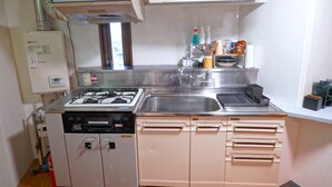 A kitchen with a gas stove, sink, and white cabinets. - El Amarillo Self Check-in Hostel (Fukushima)