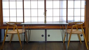 A room with a low table and two chairs, a large window with a grid pattern, and a vase with flowers on the table. - El Amarillo Self Check-in Hostel (Fukushima)