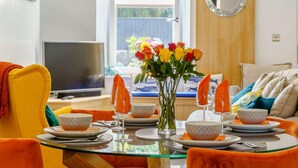 A dining area with a glass table, orange chairs, and a vase of flowers. - 3 Bed in Porthcawl (oc-85193) (Drenewydd yn Notais)