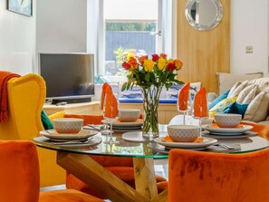 Ein Essbereich mit einem Glastisch, orangefarbenen Stühlen und einem Blumenarrangement.