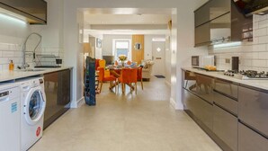 A modern kitchen with built-in appliances, a dining area with orange chairs, and a laundry machine. - 3 Bed in Porthcawl (oc-85193) (Drenewydd yn Notais)