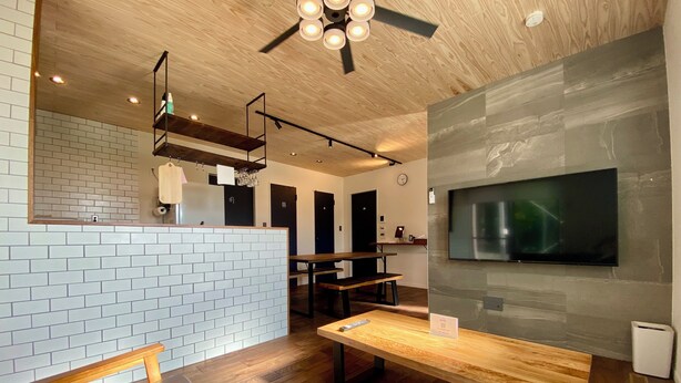 A modern interior with a wooden ceiling, a brick wall, a wooden bench, a table, and a mounted TV. - Ishigaki Villa Musubu (Ishigaki)