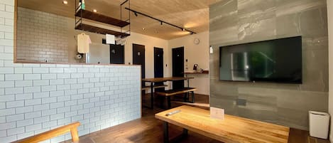 Um interior moderno com teto de madeira, parede de tijolo, um banco de madeira, uma mesa e uma TV fixada na parede.